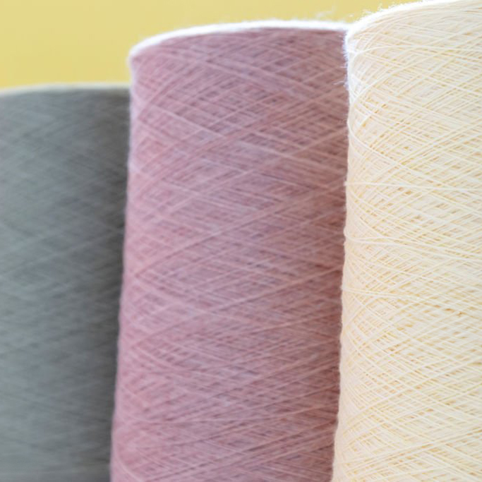 Pastel color bobbins of wool yarn for hand and machine knitting on a yellow background.